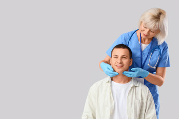 Female endocrinologist examining thyroid gland of man on light background
