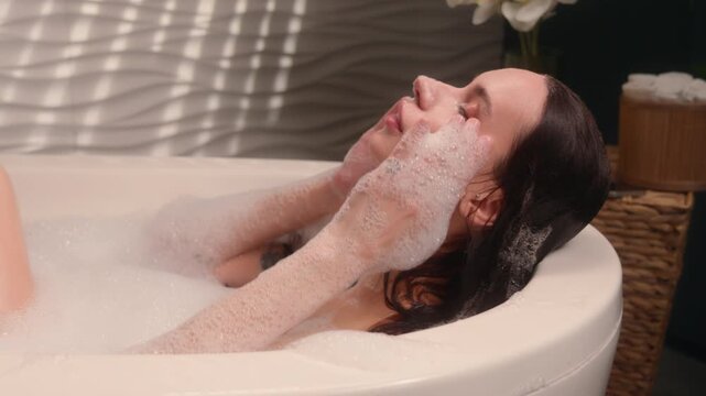 Relaxing Caucasian woman female girl lady emerge from hot warm water enjoying foamy bath at home bathroom bathtub washing head hair bathing spa stress recreation hygiene procedure body care routine