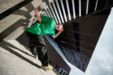 Breakdancer in green shirt strikes pose on urban steps, defying gravity with stylish move against...