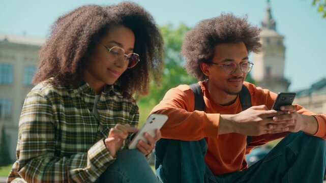 African American man guy male student boyfriend couple girl girlfriend woman female two students buddies friends siblings together outdoors in city using mobile phones dependence social media addict