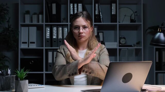 Unhappy Caucasian young adult woman showing stop sign with crossed arms in disagreement, protection or restriction while working in the office.