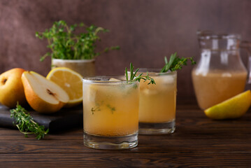 Fototapeta premium Pear lemonade with rosemary, thyme and ice on a wooden table. Healthy drink, sugar and alcohol free.