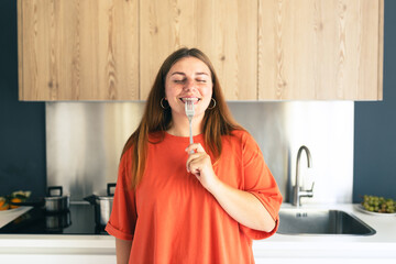 Portrait of excited hungry young woman holding fork in her mouth, biting and dreaming about...