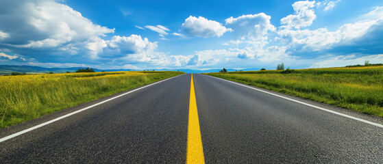 A scenic view of a long, empty road stretching into a sunny sky, surrounded by lush green fields and dramatic clouds.