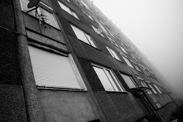 A grayscale image capturing the imposing facade of an urban high-rise shrouded in dense fog with a...