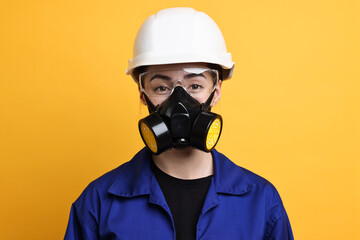 Worker in respirator, protective glasses and helmet on orange background