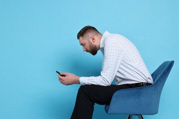 Man with poor posture sitting on chair and using smartphone against light blue background, space...