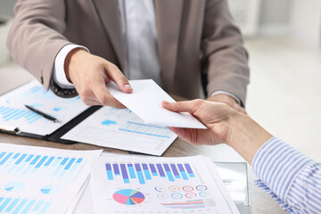 Boss giving salary in paper envelope to employee indoors, closeup