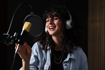 Vocalist with headphones singing into microphone in professional record studio