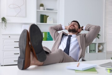 Smiling businessman with hands behind his head holding legs on table in office. Break time