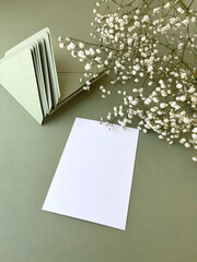 Invitation or greeting card mockup with olive envelopes and natural white gypsophila flowers, copy space. White blank wedding invitation with floral decor