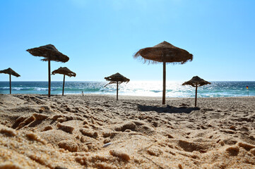 Sunshades on the vacation beach with glittering sunset sea. Tropical sunbathing and relaxation....