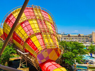 There is a large and wide water slide, trees and buildings behind it.