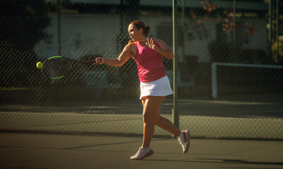 Obraz premium Sporty woman playing tennis on outdoor court hitting the ball