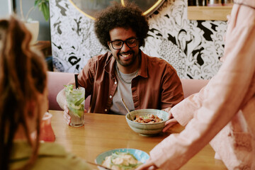 Person with curly hair smiling while talking to friends at vibrant cafe Enjoying refreshing beverage while sitting with friends Creating lively and joyful atmosphere