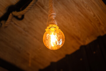 Rope ceiling lighting bulb glowing in orange warmlight shade, which is installed at living room for...