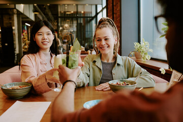 Two women sharing meal and enjoying conversation in cozy restaurant setting with plants. The room has a warm atmosphere, creating inviting ambience