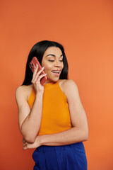 A cheerful young woman speaks animatedly on her phone, showcasing her radiant smile.