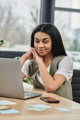 Obraz premium Smiling woman working intently on a laptop amid a contemporary workspace.