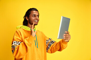 Smiling young middle eastern man waving hello calling his friends in distance against yellow studio background. Concept of human emotions, diversity, youth, modernity, study and work online. Ad