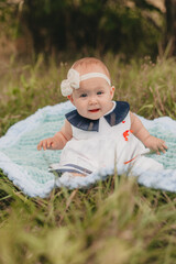 A one-year-old girl is sitting in a green meadow