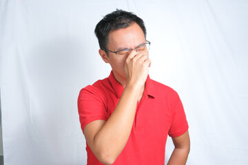 A young Asian man wearing red shirt and glasses is feeling dizzy or stressed. Isolated white background.