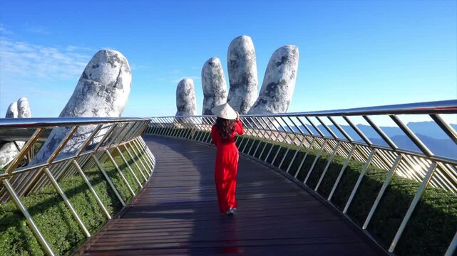 Young tourist girl in red dress walks on Golden Bridge in Ba Na Hills, Danang, Vietnam.