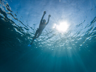 A person is swimming in the ocean with the sun shining on them