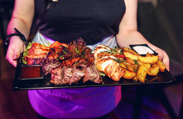 Set of delicious grilled in BBQ sauce served with vegetables on round plates and hands placed on stone table in restaurant