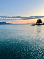 Sunset over calm waters in Lake Geneva. taken in Vevey Switzerland.  Sailboat in the water and the Swiss alps in the background.  No people.