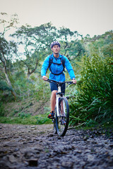 Naklejka premium Man, exercise and mountain bike on off road with helmet, plants and challenge for fitness, adventure and health. Athlete, journey and cycling outdoor in nature for workout, sports and training