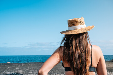 A woman in a straw hat on the breakwater, looking out to sea with a clear sky and calm sea.