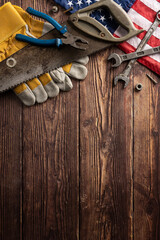 Various hand tools and work gloves with an American flag on a rustic vertical wooden background. Perfect for Labor Day themes