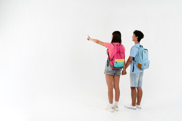 Full length rear view of high school pupils students teenagers classmates boy girl couple friends in casual with bags holding hands pointing fingers at empty copy space. Education concept