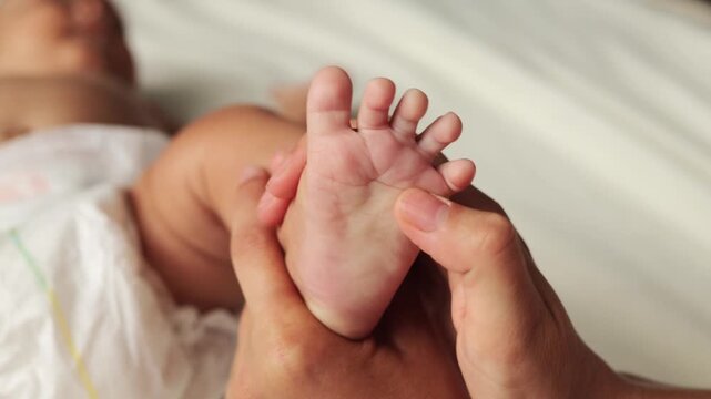 Anonymous unrecognizable mother&rsquo;s hands moved tenderly over her infant&rsquo;s tiny foot doing physical therapy for the child's orthopedic health for her daughter or son