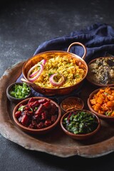 An assortment of vibrant, flavorful vegetarian Pakistani dishes, including biryani rice, served in small wooden bowls on a rustic platter, garnished with fresh herbs and onions