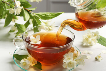 Pouring hot jasmine tea into cup on white marble table, closeup