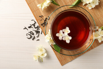 Fototapeta premium Hot jasmine tea in cup and flowers on white wooden table, flat lay. Space for text