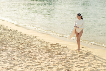 Fototapeta premium Beautiful Asian female surfer with a short board by the beach during sunset