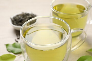 Refreshing green tea in cups and leaves on wooden table, closeup