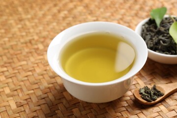 Refreshing green tea in cup, spoon and leaves on table, closeup