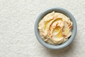 Delicious hummus with olive oil and paprika in bowl on white textured table, top view. Space for text