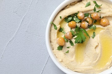 Delicious hummus with olive oil, chickpeas and parsley in bowl on grey textured table, top view. Space for text