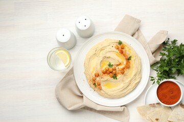 Delicious hummus with olive oil, chickpeas and paprika served on white wooden table, flat lay