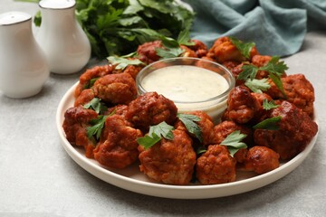 Baked cauliflower buffalo wings with parsley and sauce on light grey table, closeup