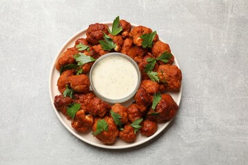 Baked cauliflower buffalo wings with parsley and sauce on light grey table, top view