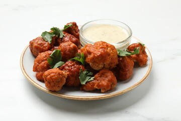 Baked cauliflower buffalo wings with parsley and sauce on white marble table