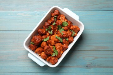 Baked cauliflower buffalo wings with parsley in baking dish on light blue wooden table, top view
