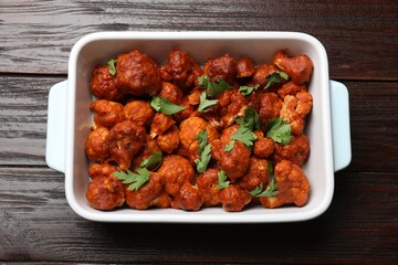 Baked cauliflower buffalo wings with parsley in baking dish on wooden table, top view