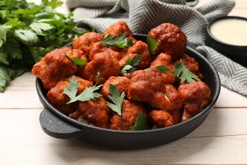 Baked cauliflower buffalo wings in baking dish and parsley on wooden table, closeup